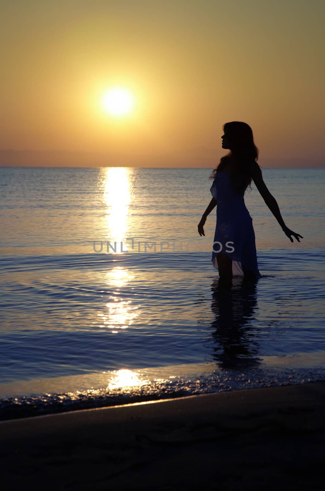 Silhouette of the serene woman standing in the water during golden sunset. Natural colors and darkness