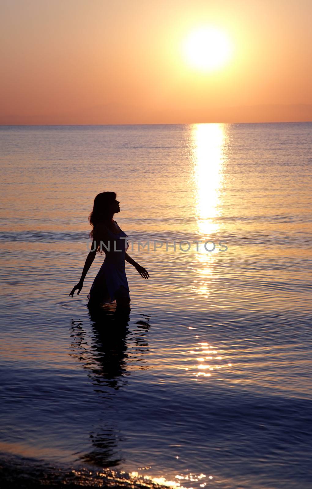 Silhouette of the woman standing in the sea water during golden sunset. Natural colors and darkness
