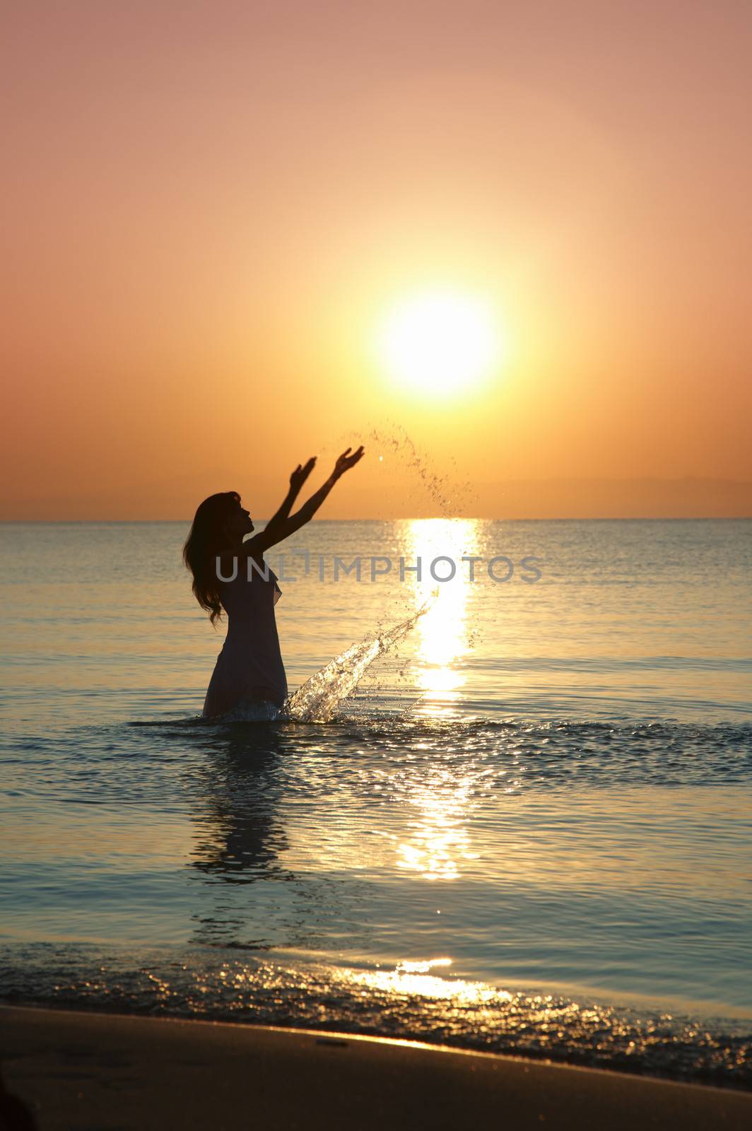 Silhouette of the woman playing with water during sunset. Natural darkness and colors
