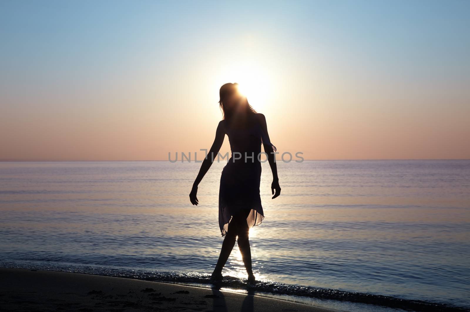 Silhouette of the lady standing at the beach during sunset. Sunlight is going through woman's hair. Natural light and colors