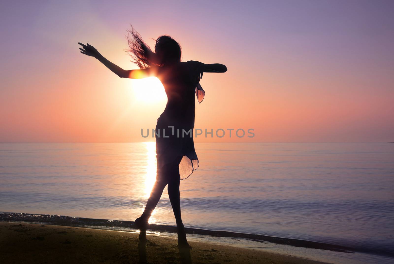 Silhouette of the woman dancing at the beach during beautiful sunrise. Natural light and darkness. Artistic vivid colors added