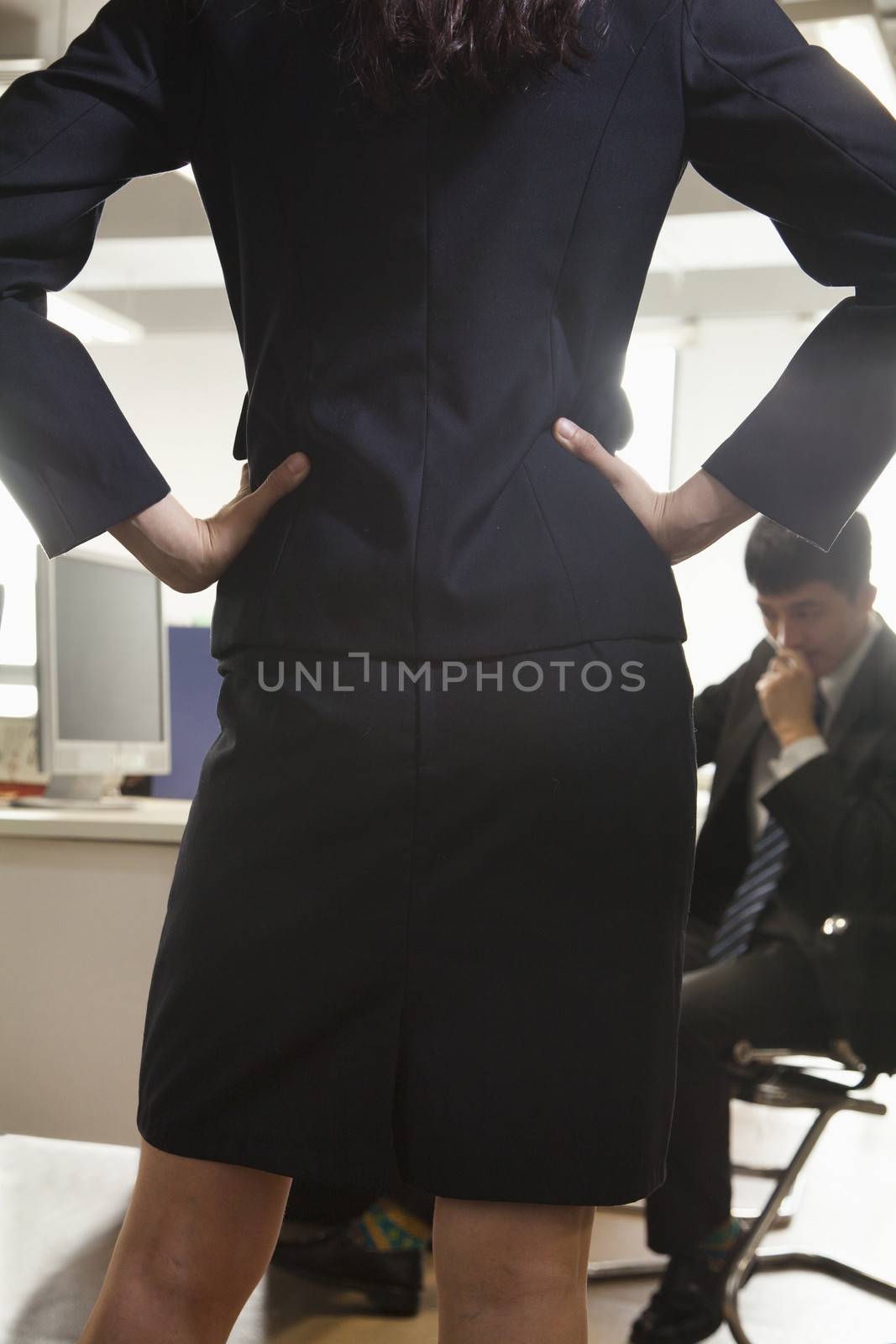 Rear view of businesswoman with her hands on hips confronting a coworker 