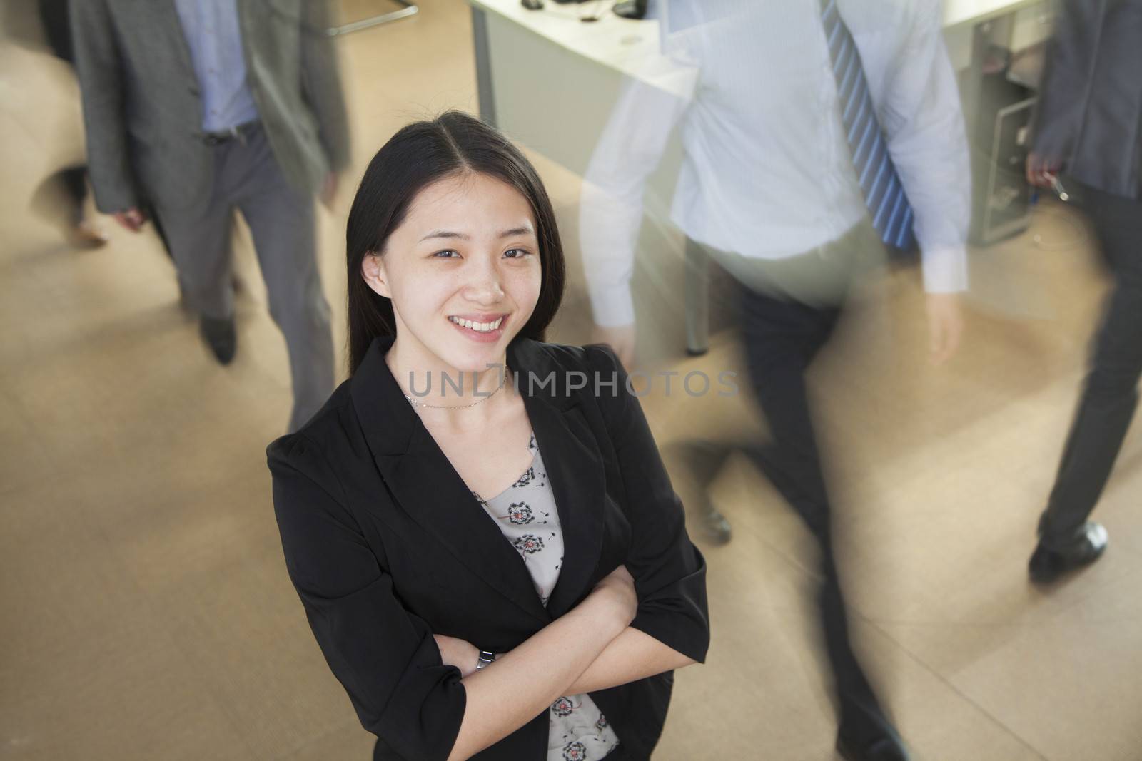 Young businesswoman smiling in the office, businessmen walking all around her by XiXinXing