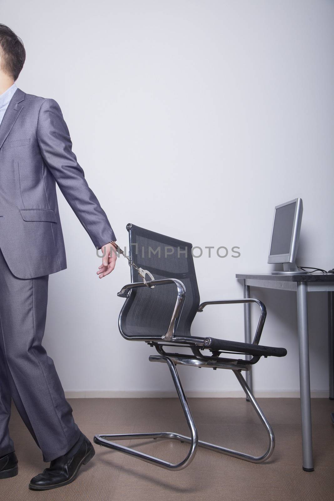 Businessman handcuffed to his office chair, walking away