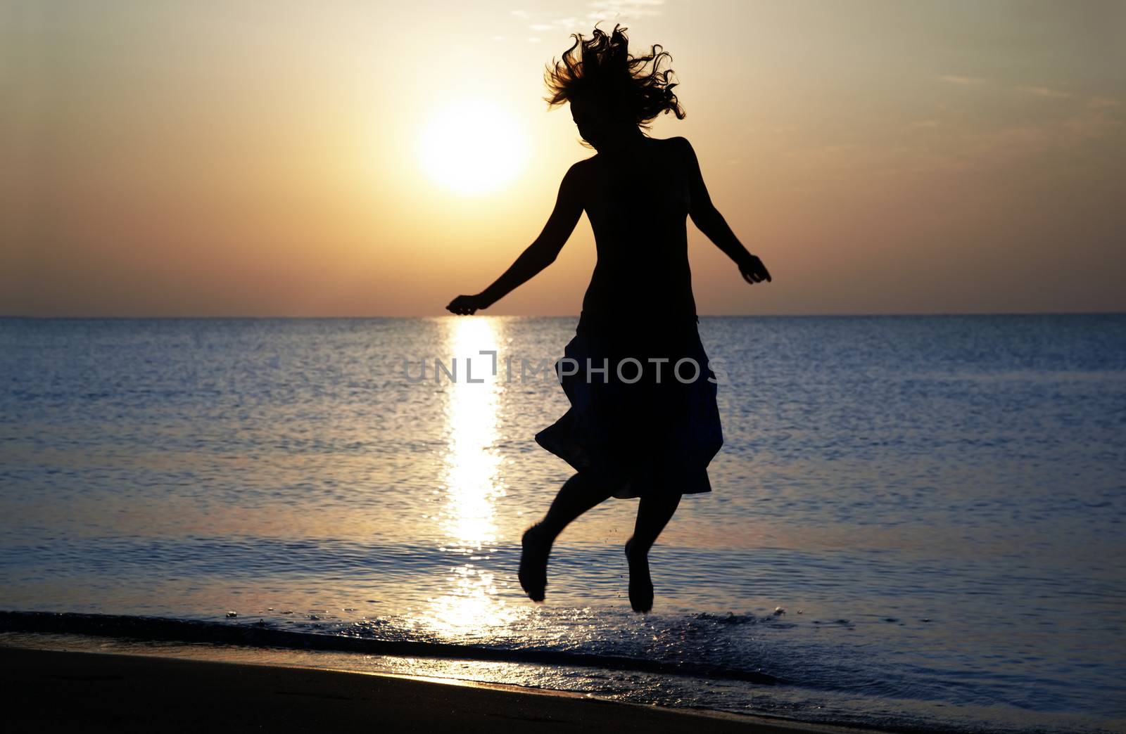 Silhouette of the happy woman jumping and dancing at the sea during sunset. Natural light and shadows