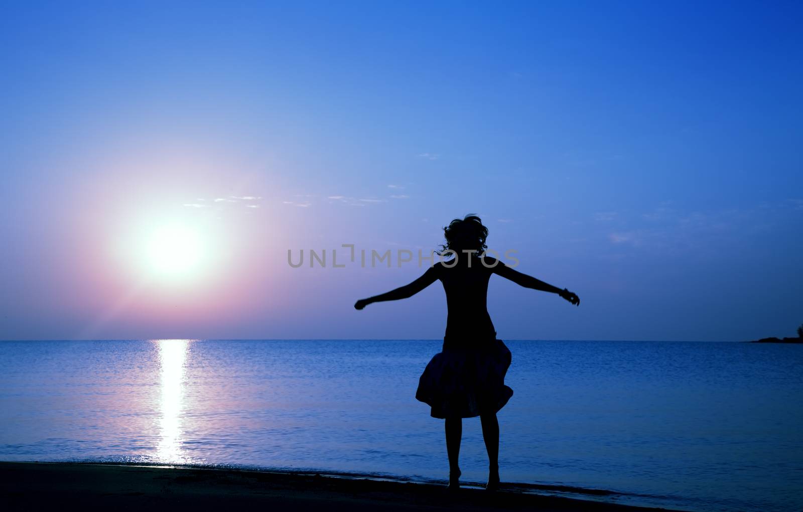 Silhouette of happy woman jumping at the beach during twilight