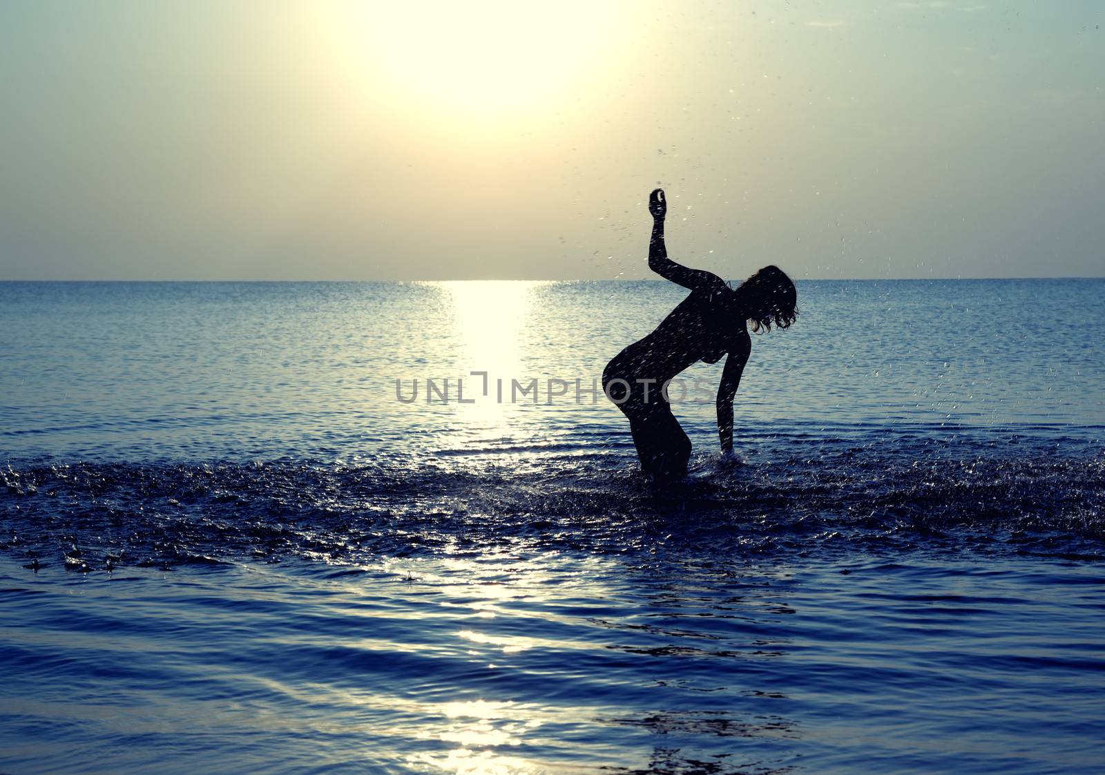 Silhouette of the happy woman playing with water at summer beach