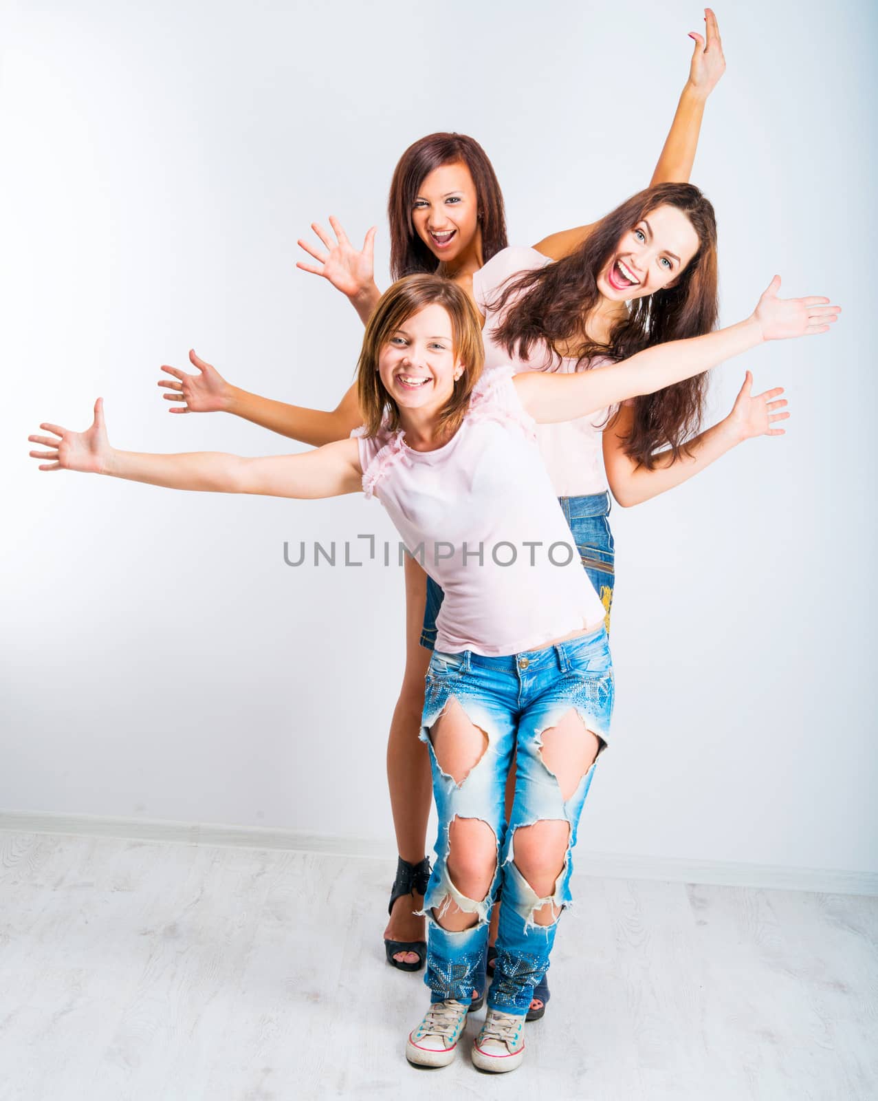 three teenage girls with hands up on light background