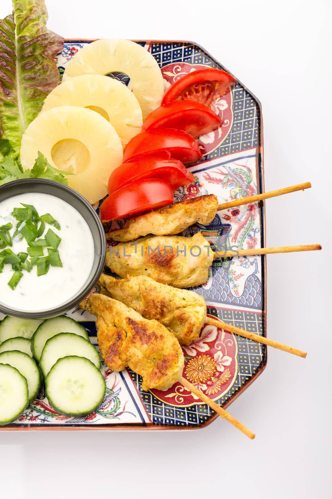 Asian food with chicken skewers, sauce, tomatoes, cucumber, pineapples and salad.