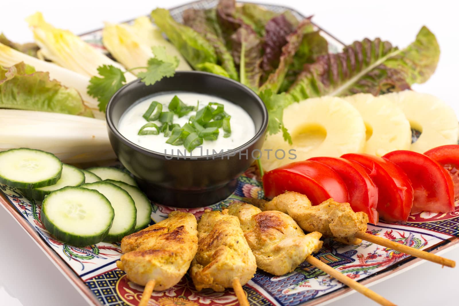Asian food with chicken skewers, sauce, tomatoes, cucumber, pineapples, endives and salad.