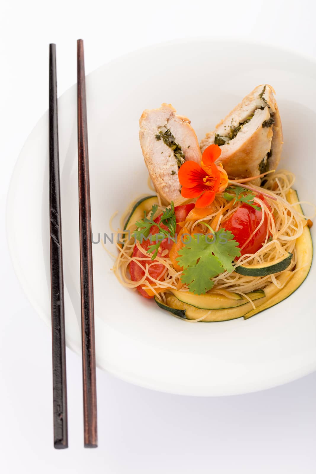 Asian food with piece of stuffed chicken, noodles, zucchini, carrots and tomatoes.