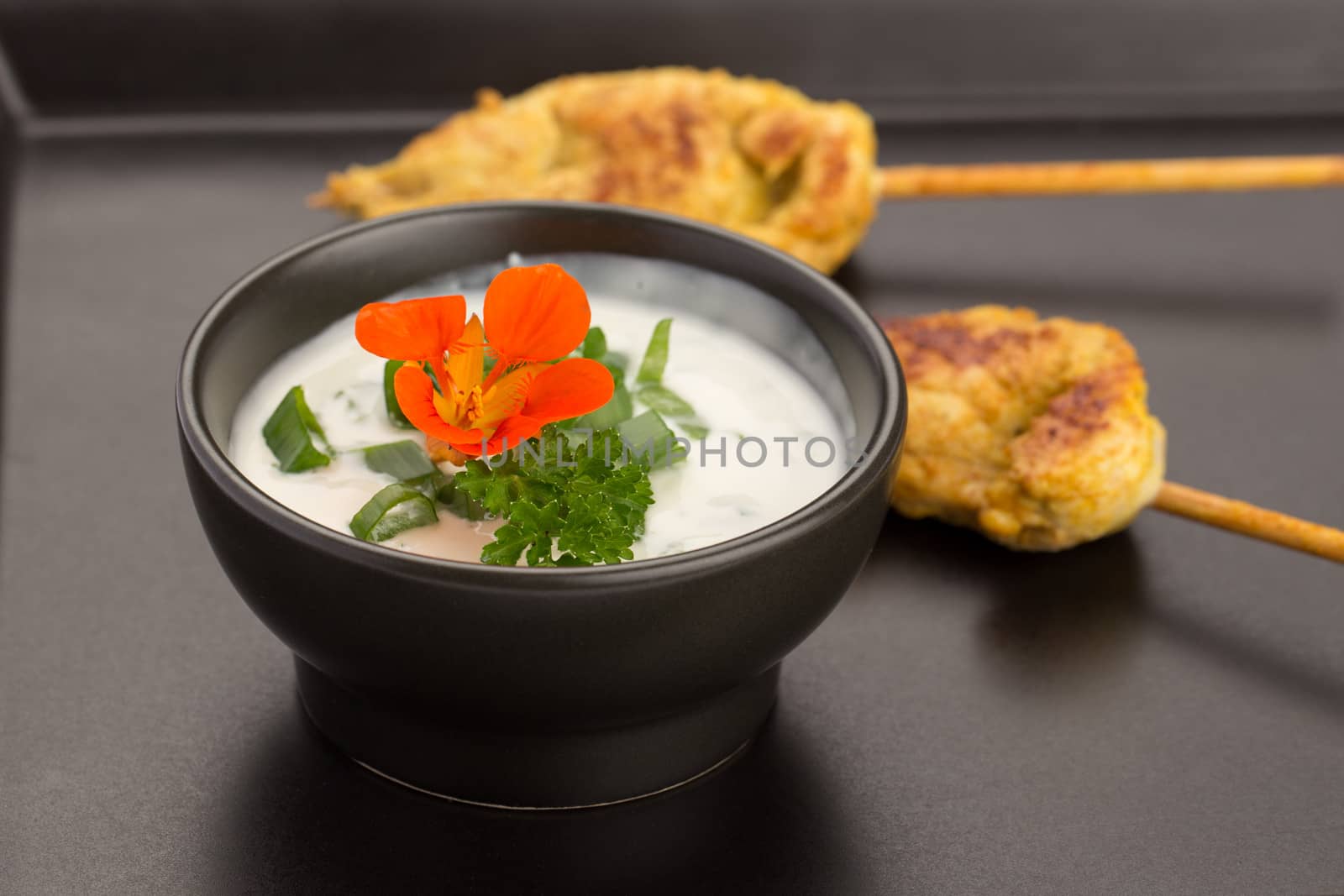 Chicken skewers and bowl of sauce on a black plate.