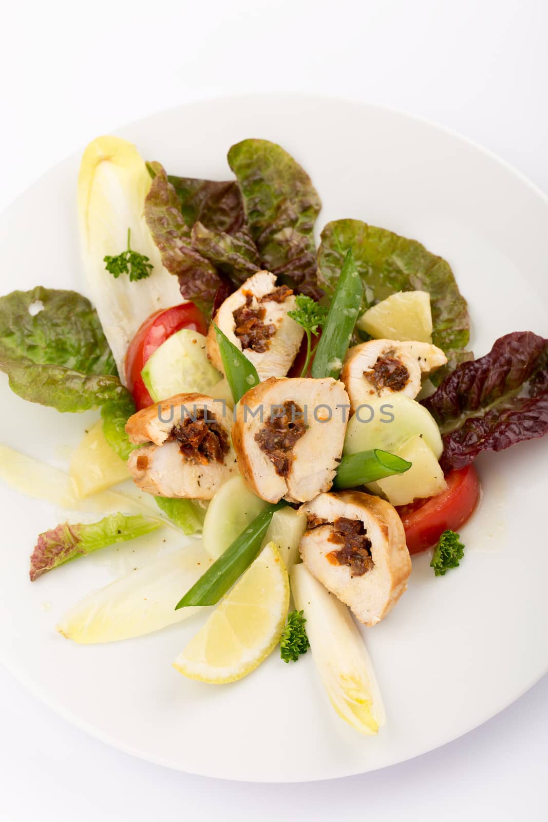 Plate of food with sliced stuffed chicken, endives, tomatoes and salad.