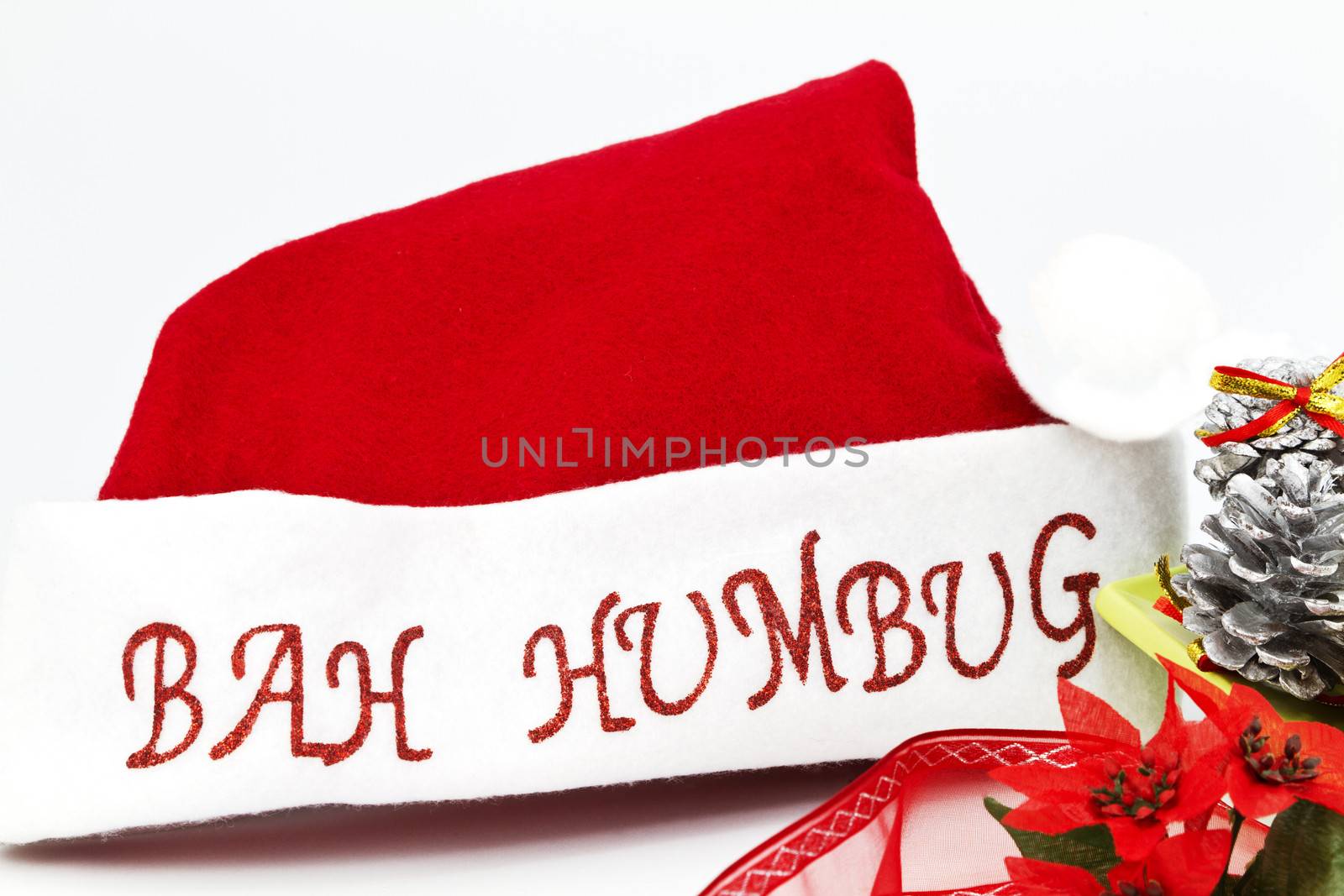 Red and white Santa Claus hat placed with silver pine cones, ribbons, and poinsetta flowers on white background.