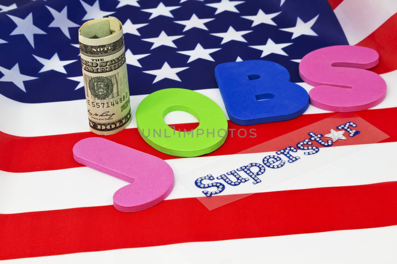 Letters spelling JOBS placed on American flag with currency and Superstar in glitter letters emphasizes critical nature of employment in today's economy and financial environment.