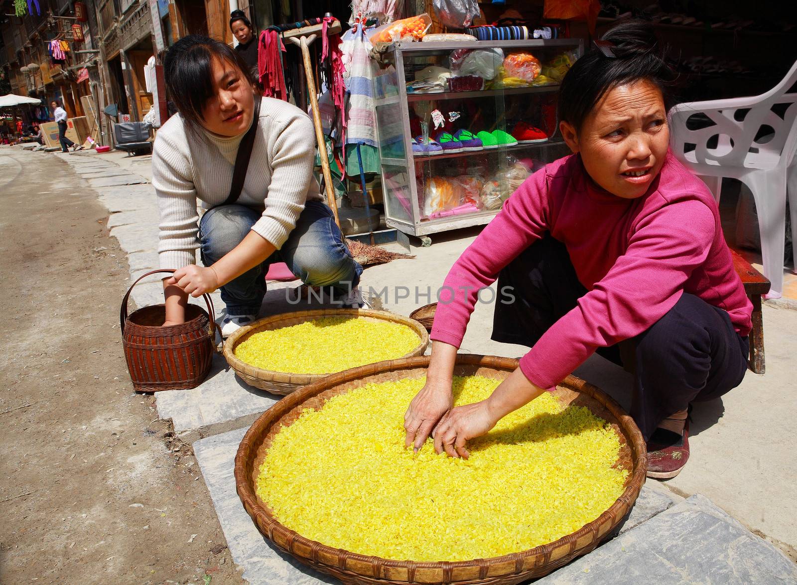 Dong ethnic women treated with rice on a street Zhaoxing Dong Village. Yellow rice is found in large wicker baskets. Zhaoxing Town, Liping County, Guizhou, China. by grigvovan