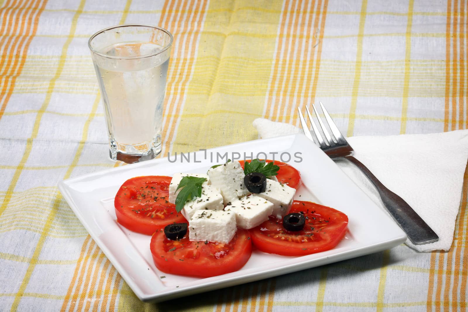 Tomato salad with feta cheese, sliced olives and glass of uzo