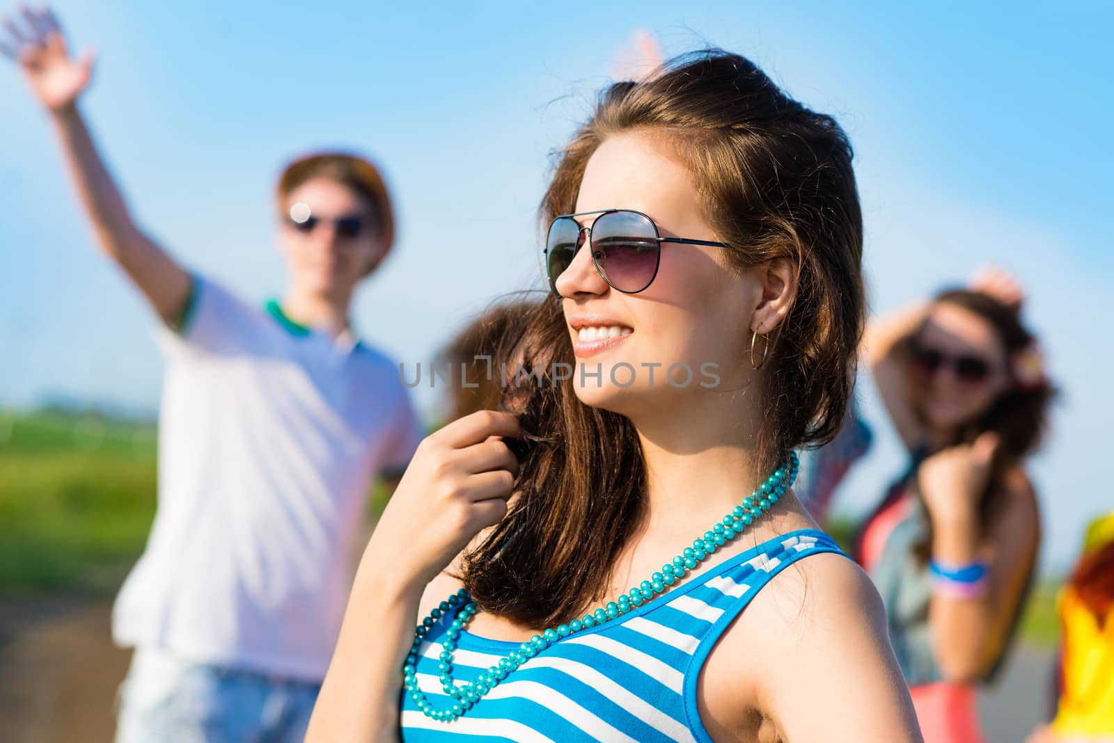 stylish young woman in sunglasses on the background of blue sky and friends