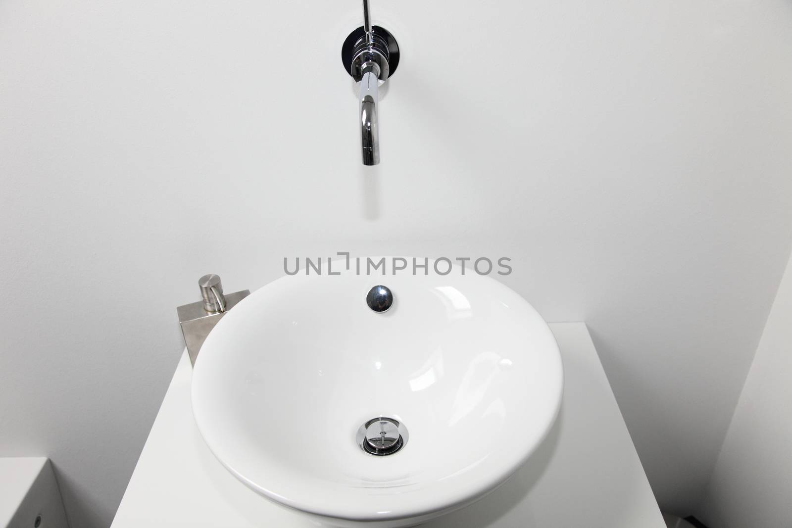 Closeup view of a modern circular ceramic handbasin and wall mounted tap in a bathroom