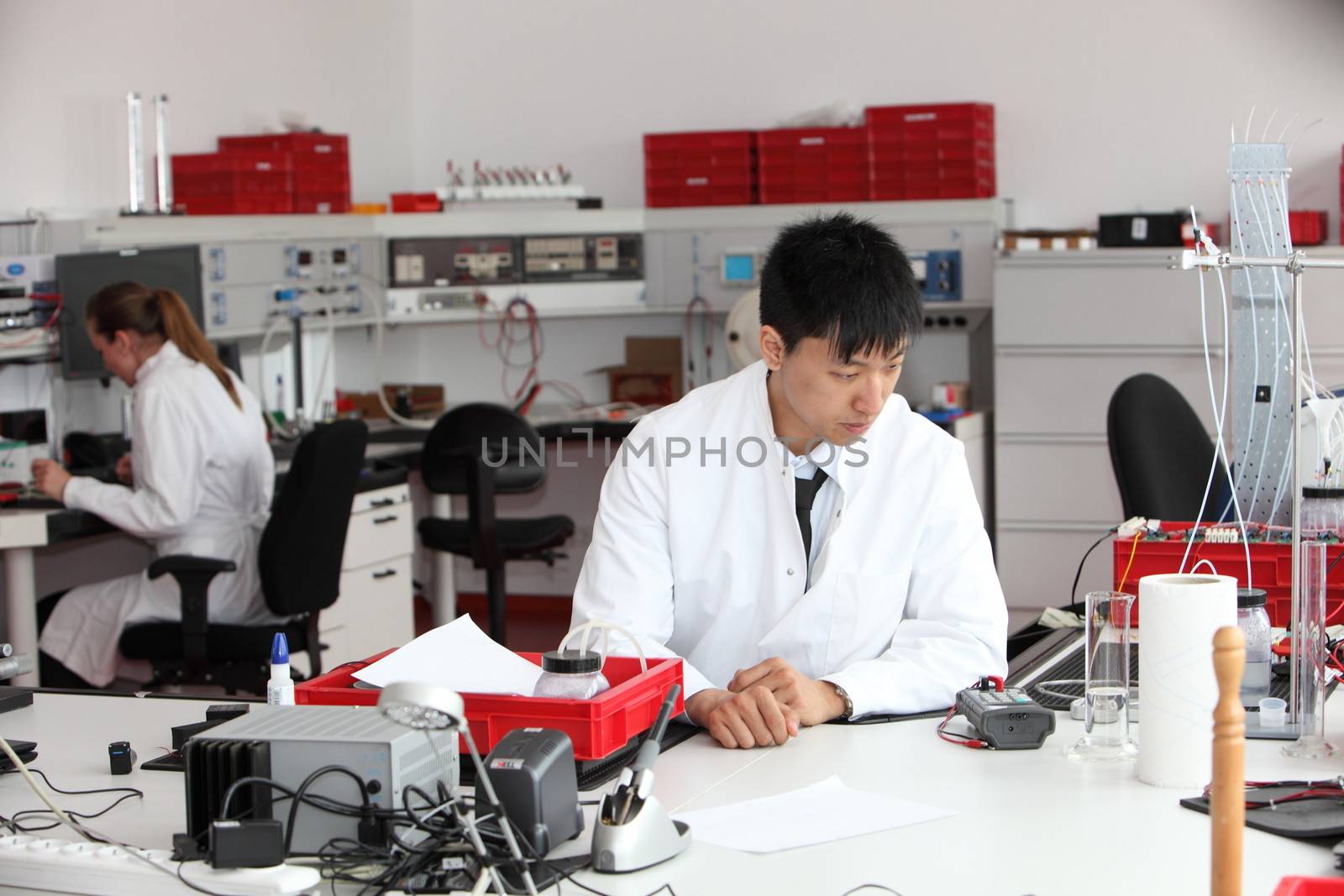Young male Asian laboratory technician seated at his desk watching a sample complete its analysis as he performs chemical tests