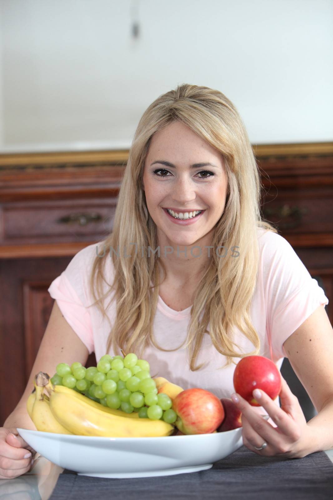 Beautiful woman enjoying a healthy diet sitting in front of a bowl of delicious fresh fruit holding a red apple in her hand