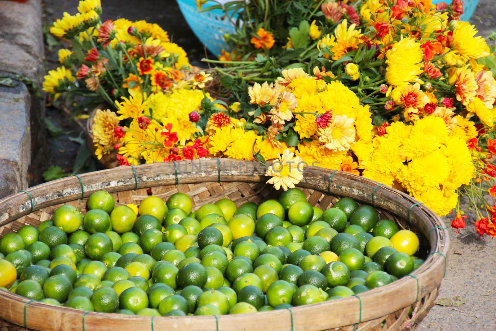 A basket full of fresh green asian limes and buquets of mixed yellow field flowers in a market in Vietnam