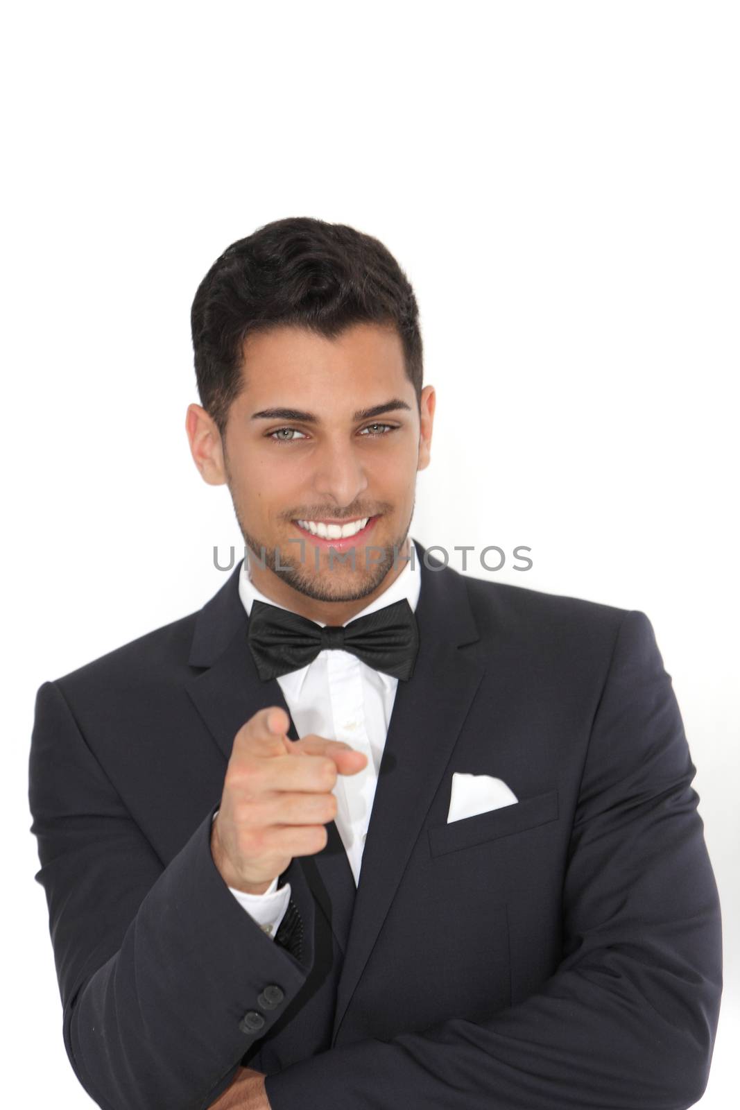 Handsome man in a tuxedo pointing directly at the camera with a friendly smile, isolated on white