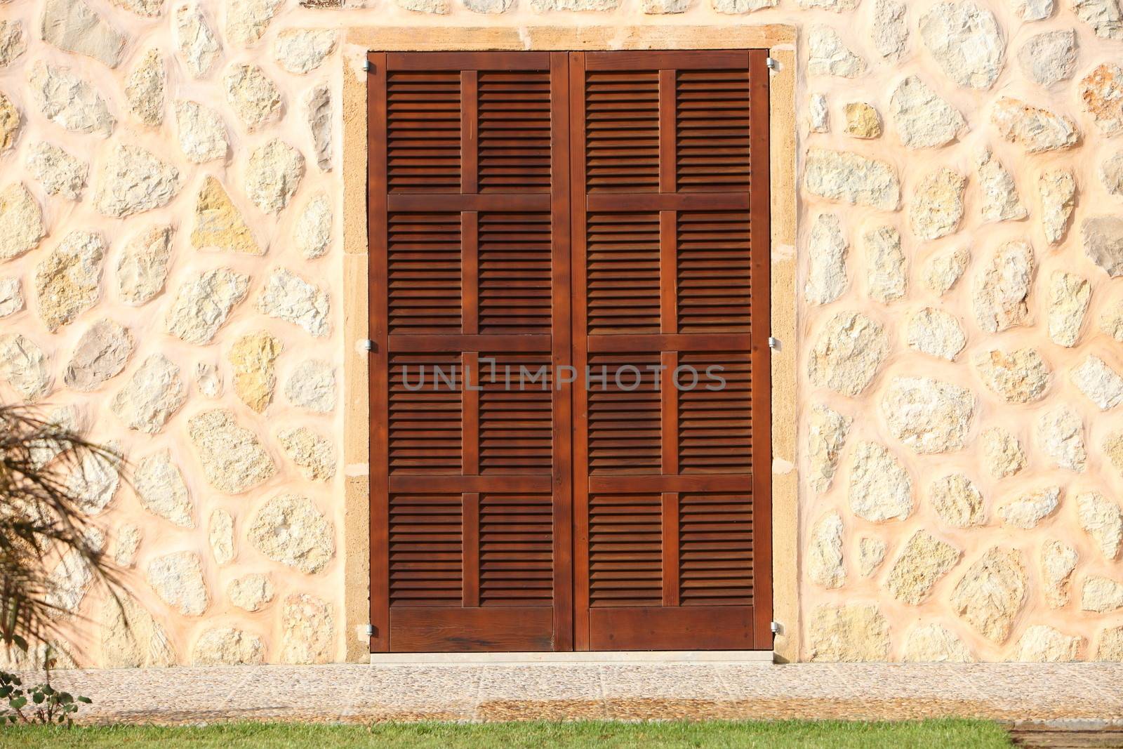 Shuttered wooden window in a stone building with walls composed of painted natural rock