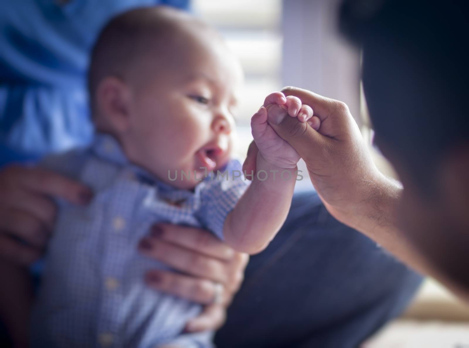 Cute Mixed Race Infant Holds Father's Thumb as Mom Looks On - Focus is on the Hand of the Baby Boy.