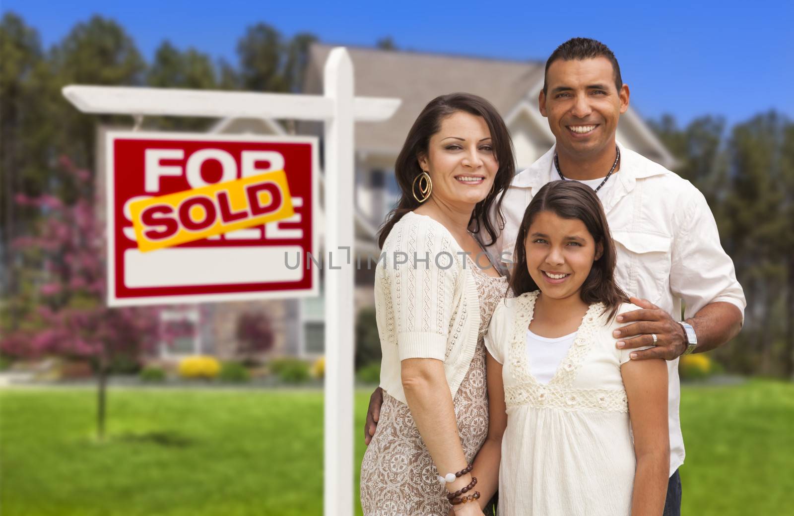 Hispanic Mother, Father and Daughter in Front of Their New Home with Sold Home For Sale Real Estate Sign.