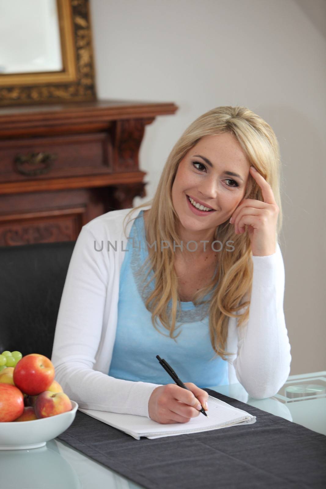 Beautiful young woman sitting in her dining room at the table thinking as she writes her correspondence