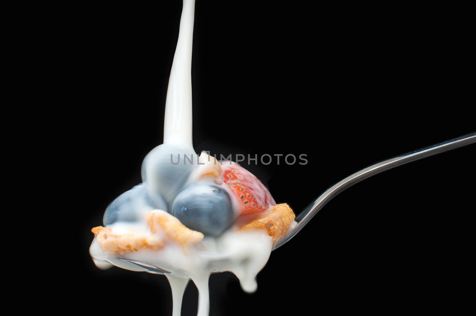 Milk pouring over a spoon with breakfast cereal and berries  