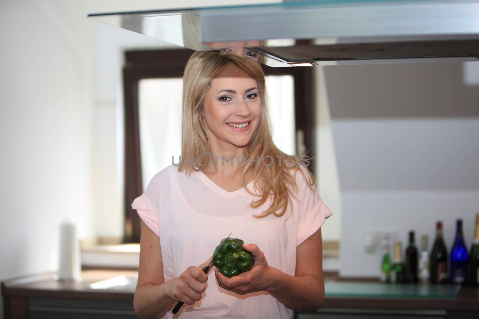 Pretty friendly blond woman preparing dinner in the kitchen slicing a green pepper with a knife
