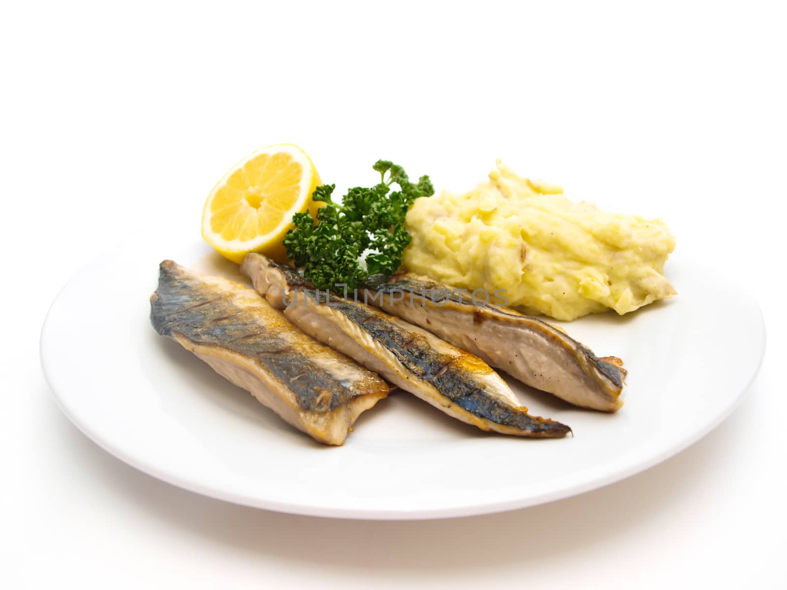 Fried mackerel on white plate with half lemon, green parsley and mashed potatoes
