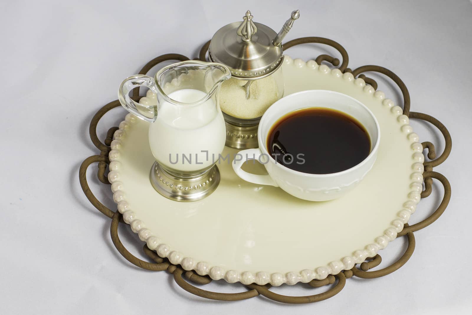 A fresh cup of coffee sitting on a decorative plate with cream and organic sugar.