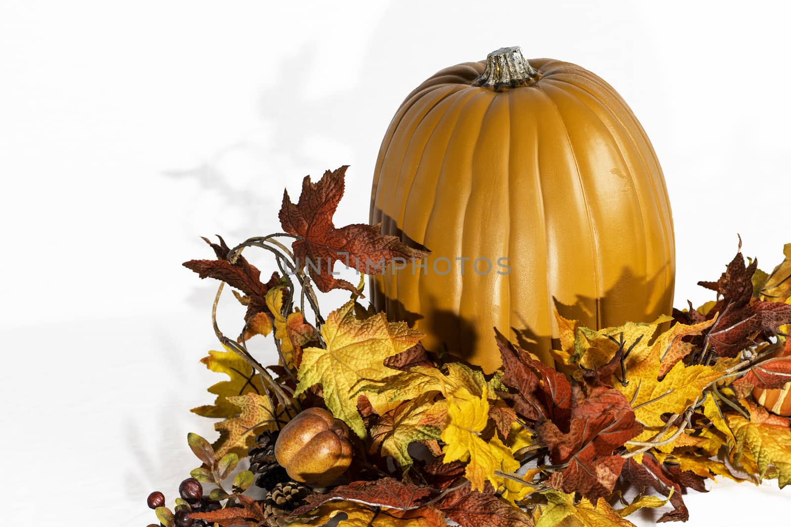 A pumpkin sitting behind a group of autumn leaves.