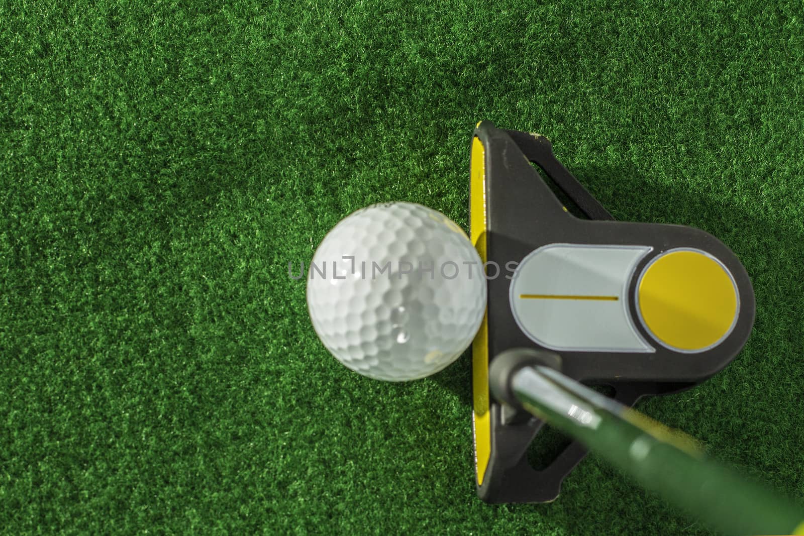 A golf ball about to be struck by a black and yellow putter.