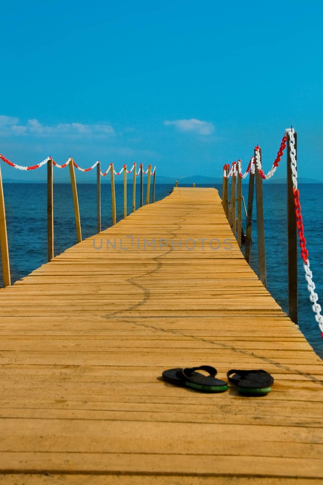 slippers on wooden peer with blue sea by mturhanlar