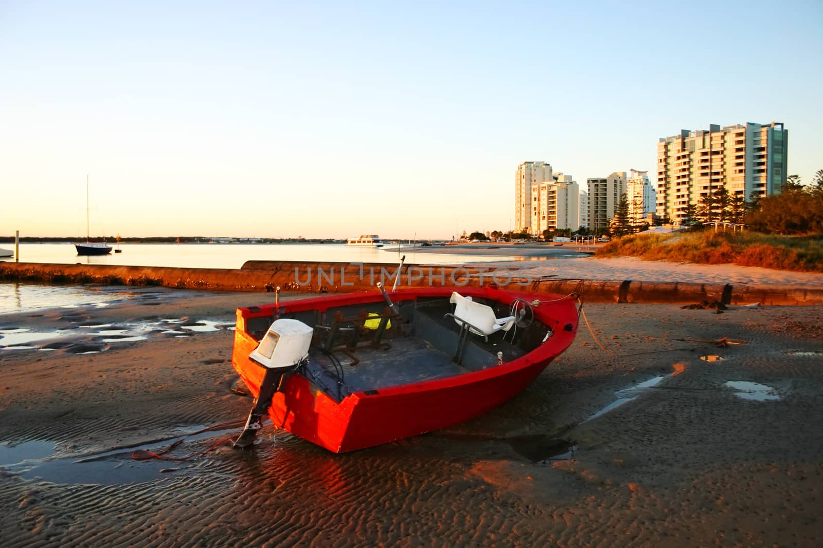 Battered old red dinghy with outboard motor lies on the beach at dawn.