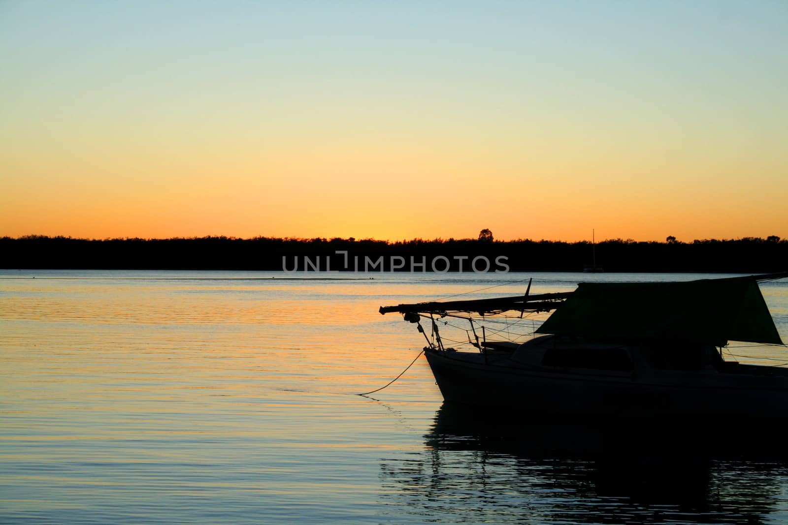 Sun rises over still waters with yacht at rest.