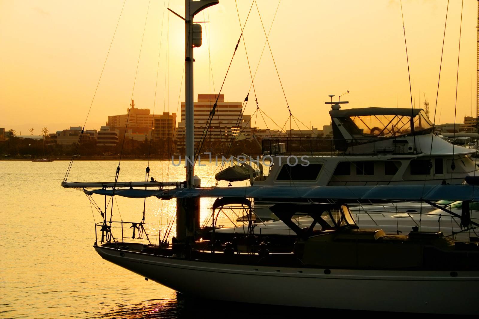 Yachts moored at marina with the sun setting over the skyline.
