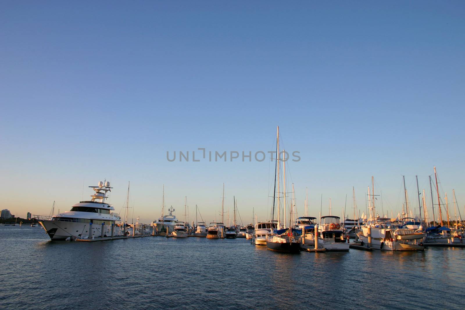 Yachts cruisers and a superyacht all moored at marina.