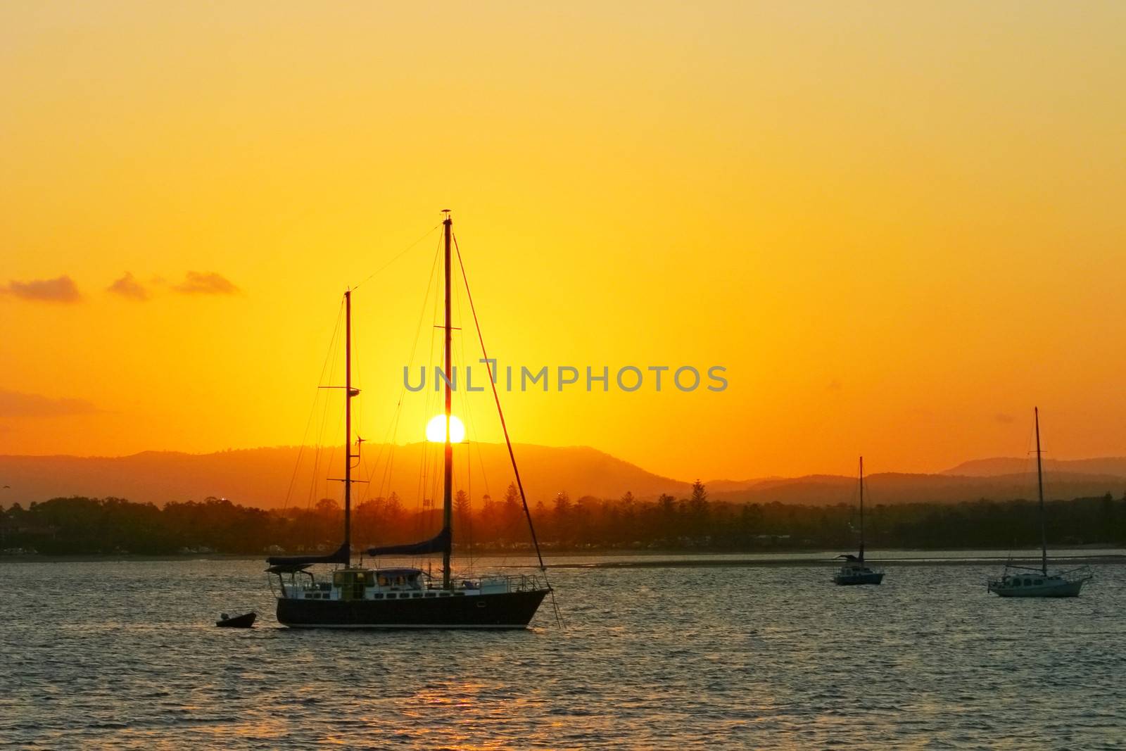Yachts anchored at sunset with a blazing sun and sky.