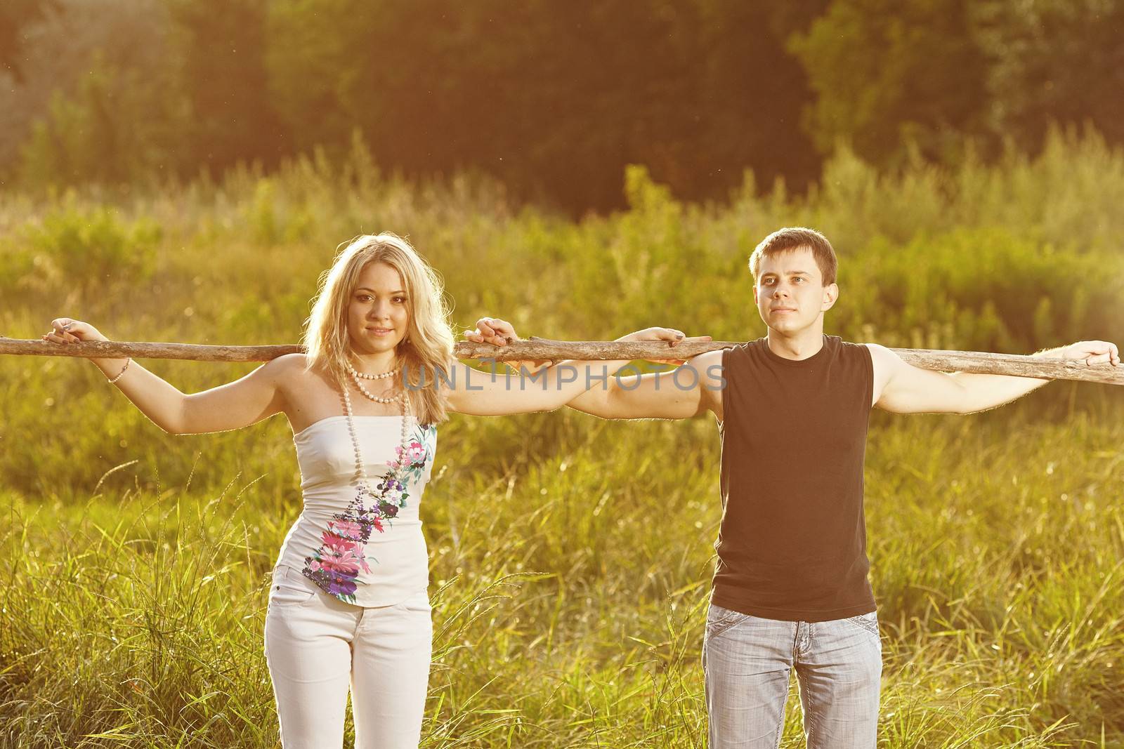 Young couple support each other, holding on to a tree on a background of green