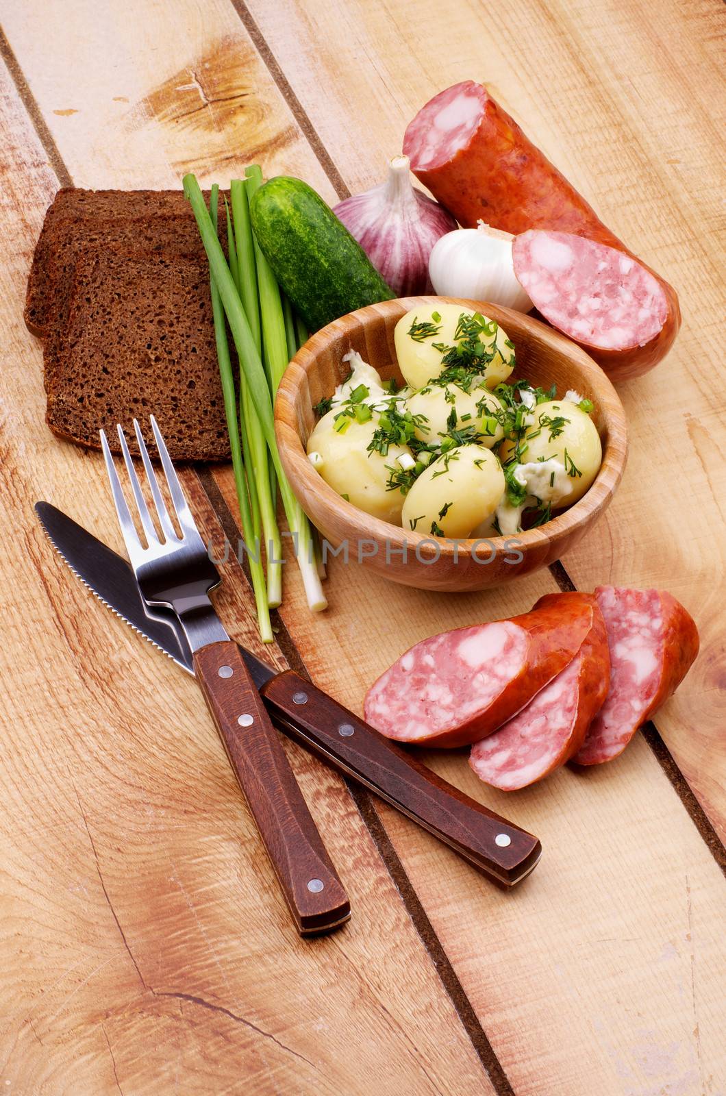 Arrangement of Boiled Potato, Greens, Homemade Smoked Sausage and Whole Grain Bread with Fork and Knife with Wooden Handles closeup