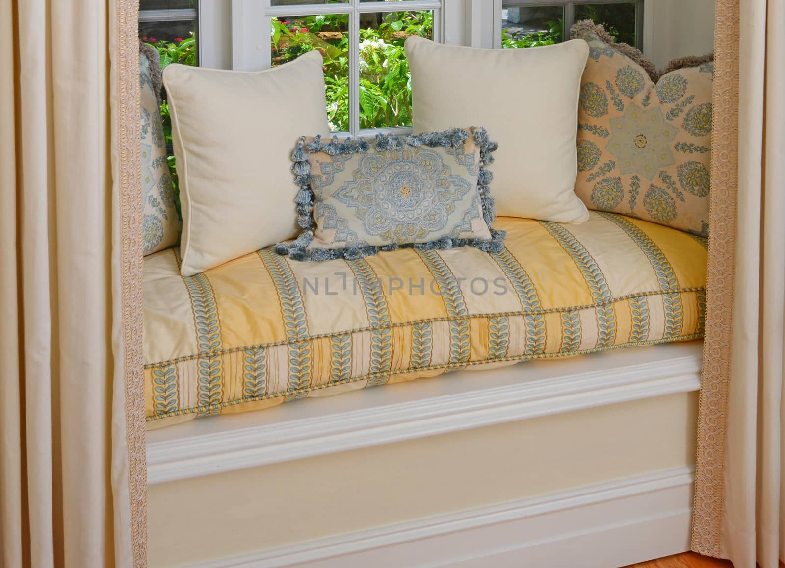 A seating area in a bay window with decorative pillows and cushions in a window seat

