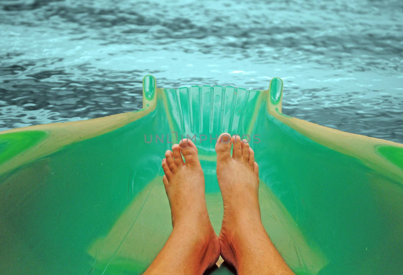 A pair of feet on a water slide about to land in a refreshing pool