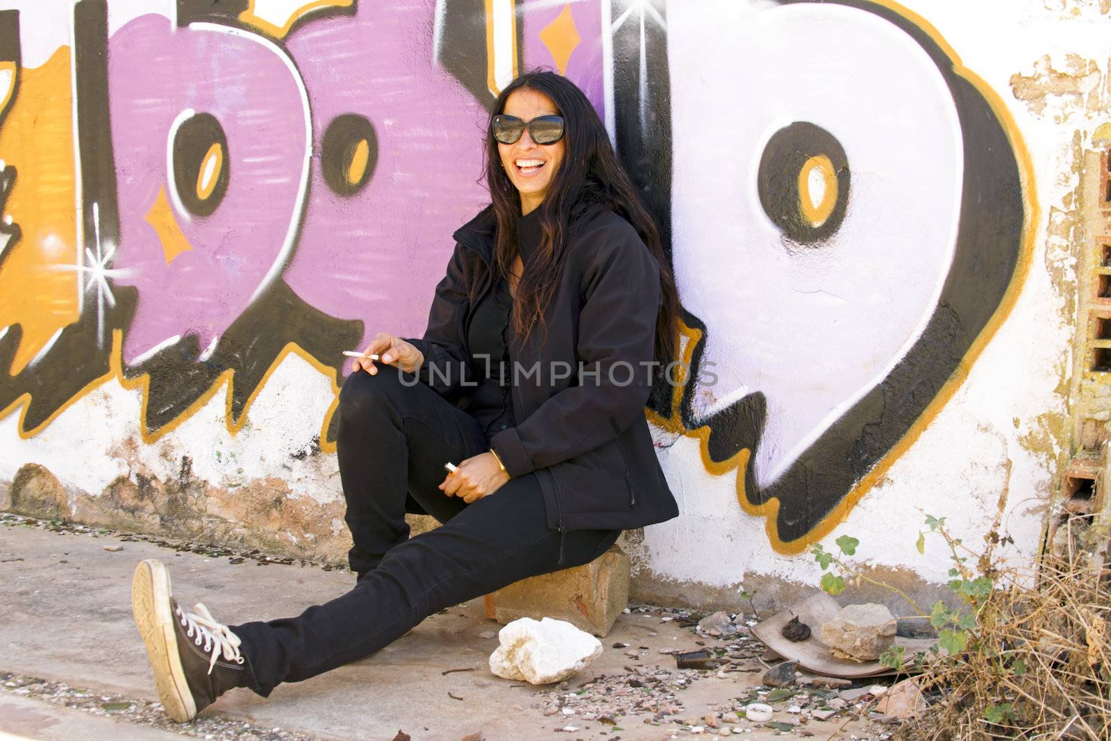 Happy smoking woman sitting in front of a graffiti wall
