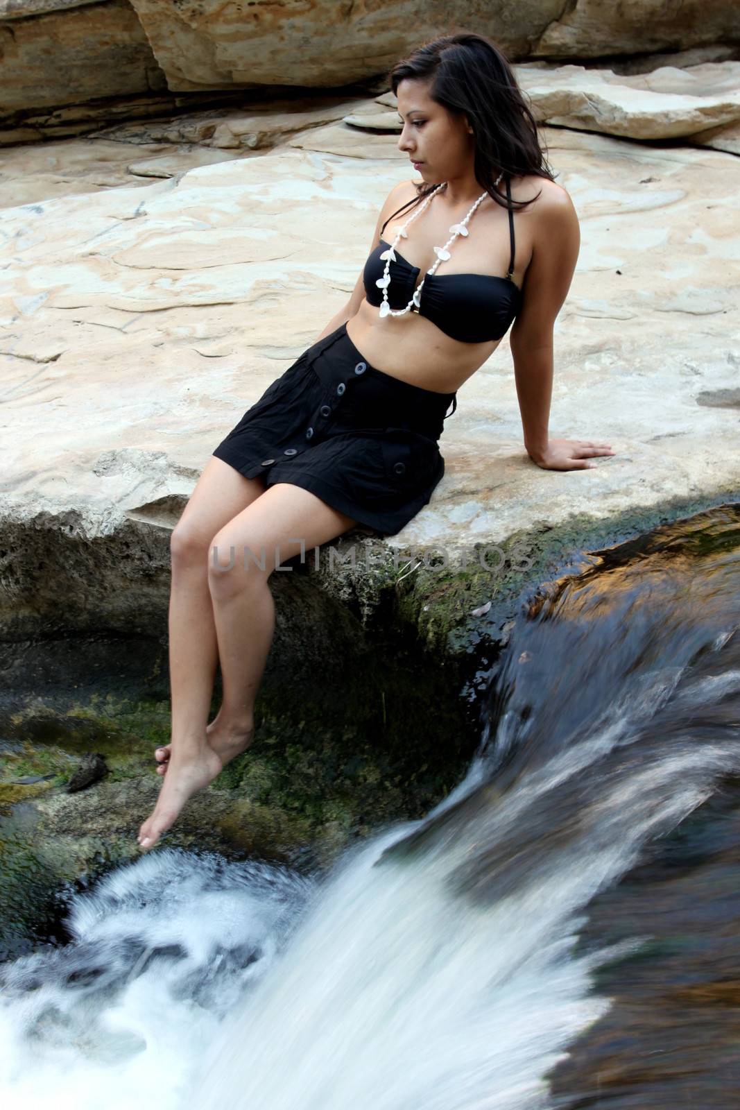 Hispanic woman with bikini sitting next to a waterfall.