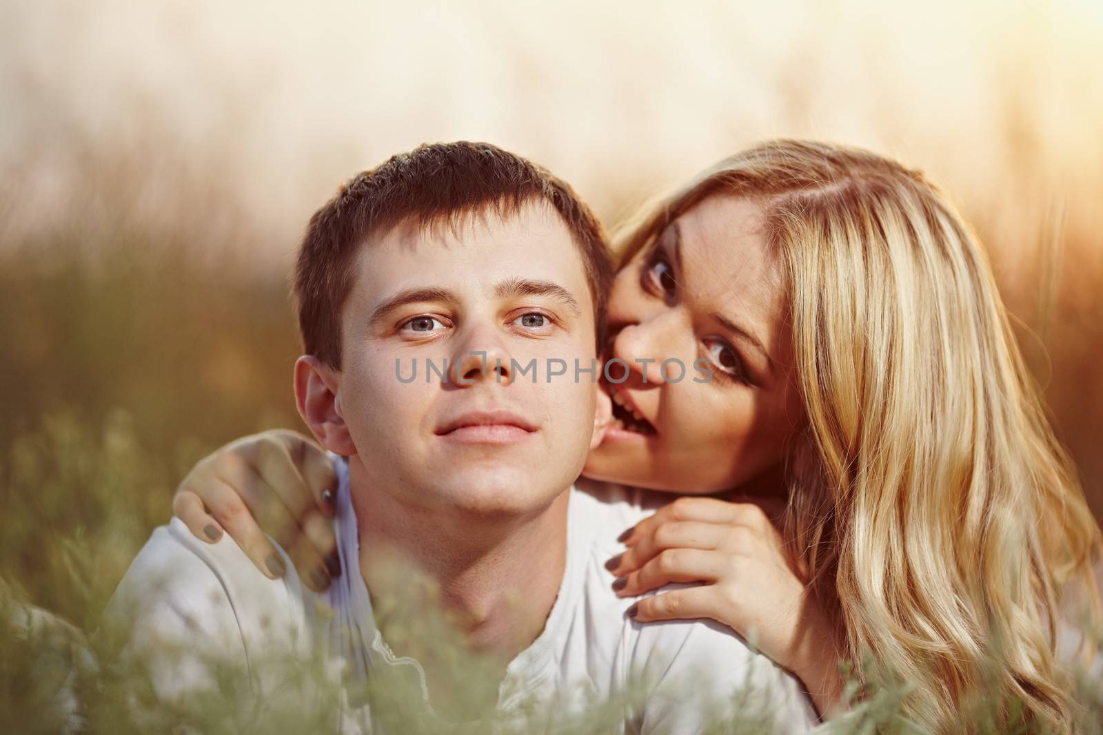 oung couple lying on the sunset background. Man bites woman's ear